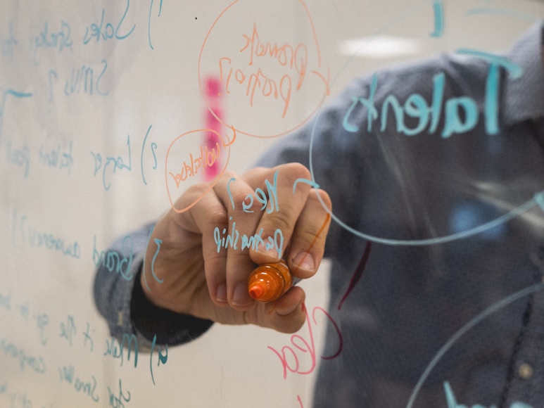 Photo of a hand writing innovative ideas on a clear marker board.