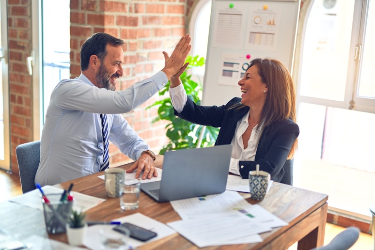 Photo of two people sitting at a work desk and high-fiving, symbolizing customer success.